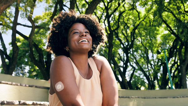 Woman with a Dexcom G7 Glucose Monitor on her arm sitting outdoors with trees in the background