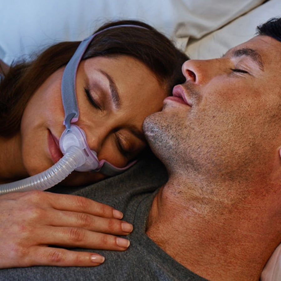 Person using a CPAP machine with a partner lying next to them.