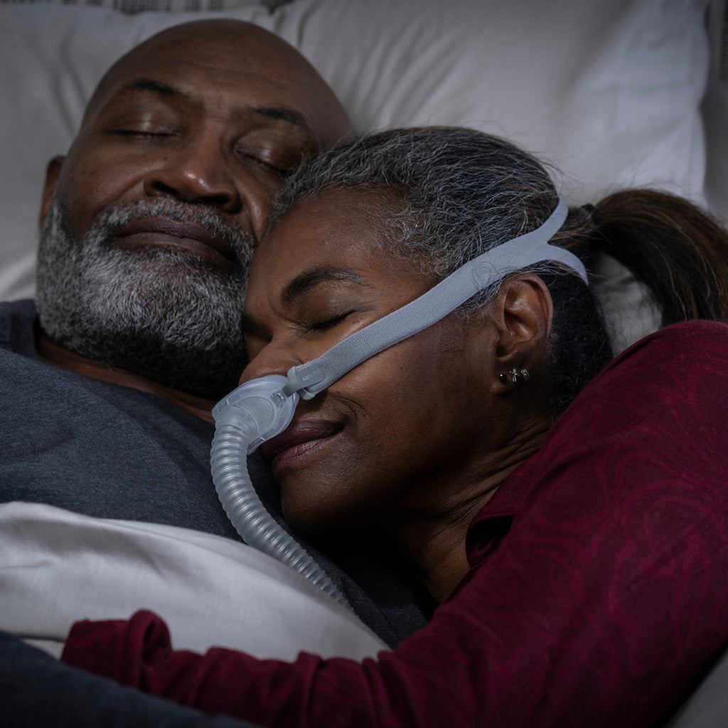 Two people lying in bed with one using a CPAP machine.