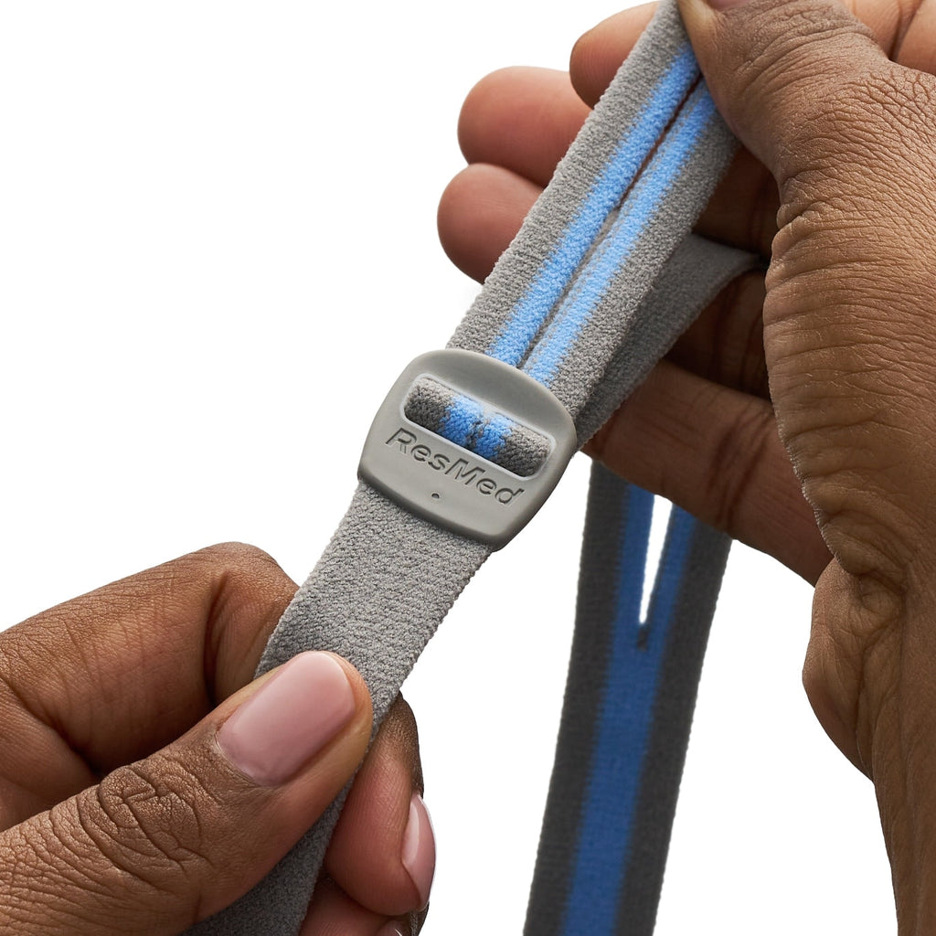 Gray and blue strap with ResMed logo held by a hand on a white background