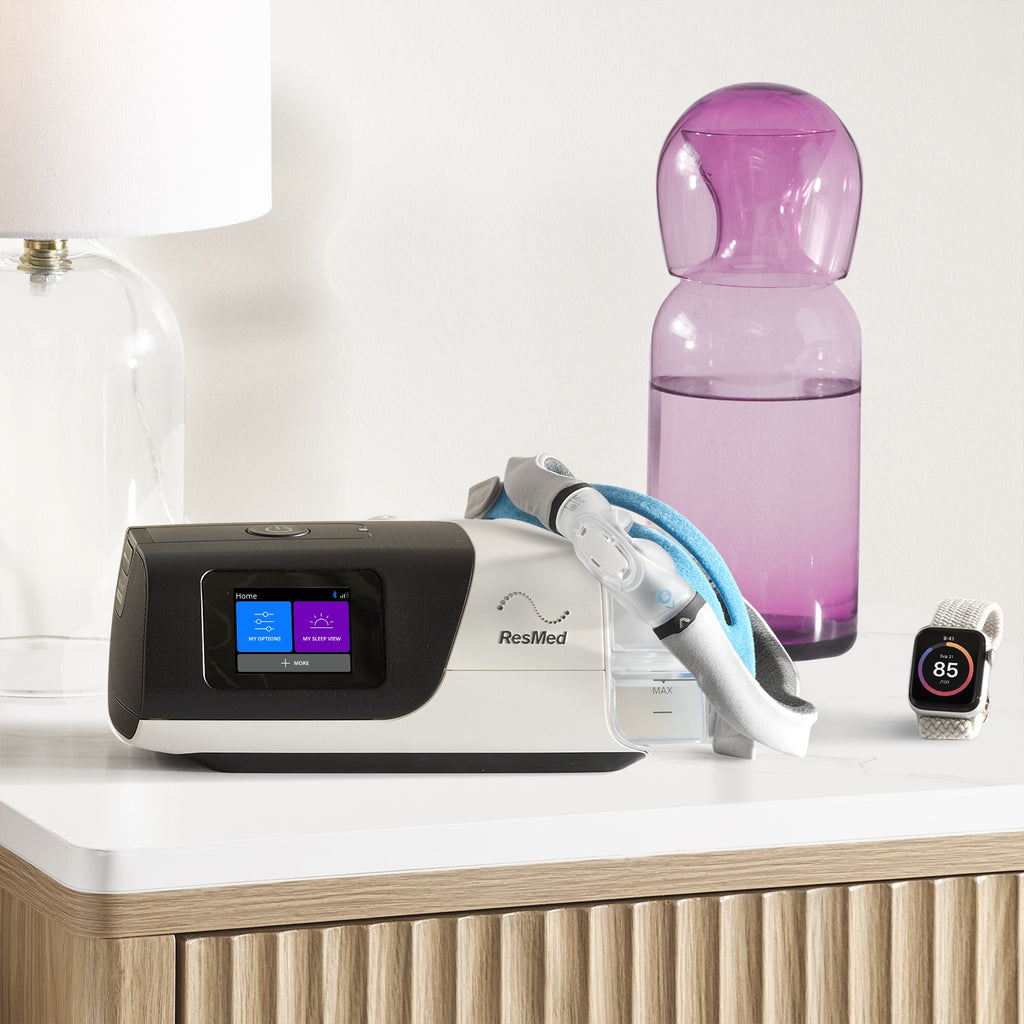 ResMedsleep therapy device on a nightstand with a pink water bottle and smartwatch.