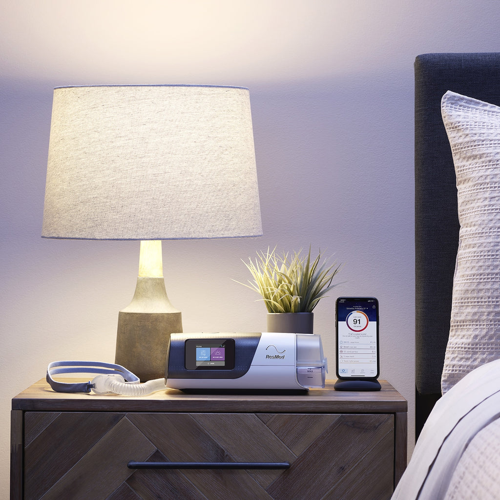 Airsense 11 Autoset on a wooden nightstand with a lamp and books in a bedroom setting