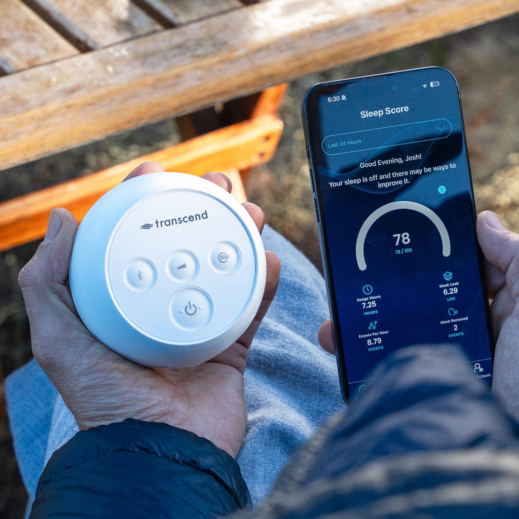 Person holding a Transcend sleep device and a smartphone with sleep tracking app outdoors.